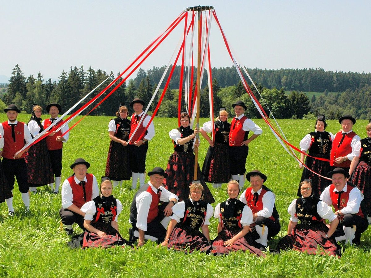 Die Erwachsenentanzgruppe in Tracht mit Bändern um einen Maibaum auf einer Wiese